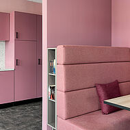 Büroaufenthaltsraum mit offener Küche und Sitzgelegenheit in dunklem rosa